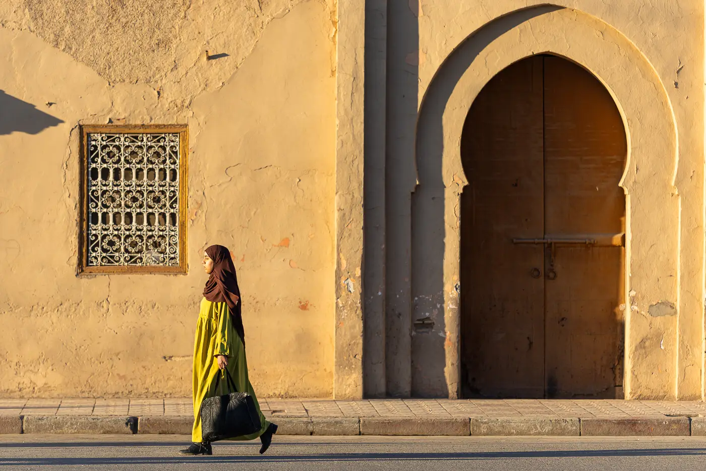A woman walking past a wall in Taroudant during golden hour